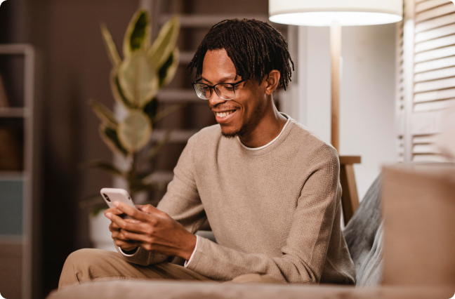 homem negro com molettom bege mexendo no celular e sorrindo